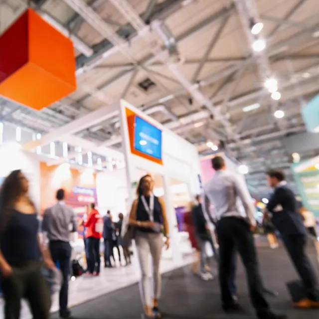 Besucher auf einer Messe in einer großen Halle mit Ständen