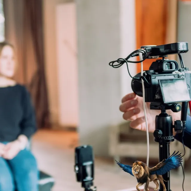 Kamera auf Stativ bei einem Interview, unten ein kleiner geflügelter Löwe