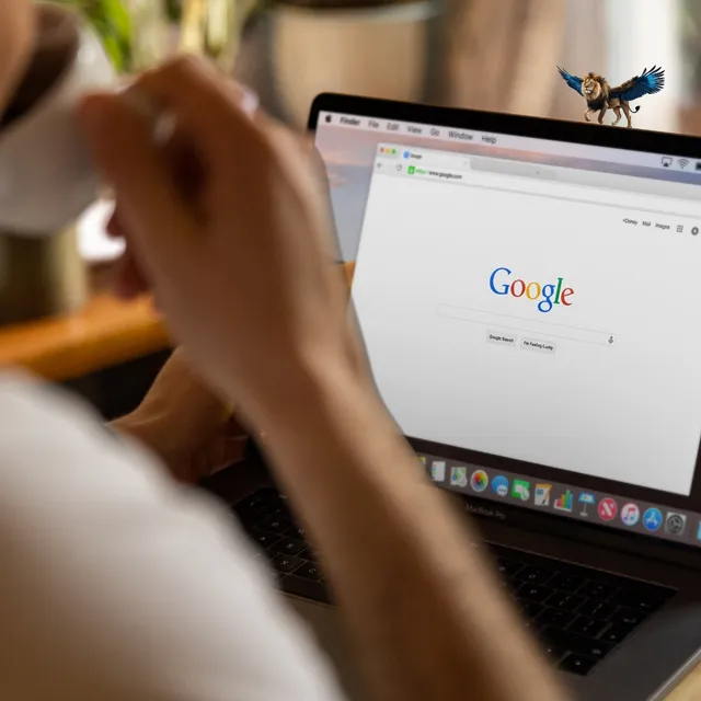Person bedient einen Laptop mit der Google-Suchseite, oben rechts ein kleiner geflügelter Löwe