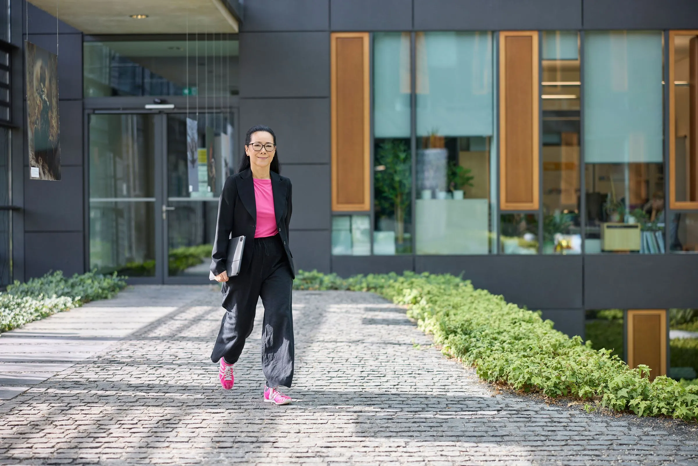 Frau in dunklem Anzug geht vor einem modernen Bürogebäude